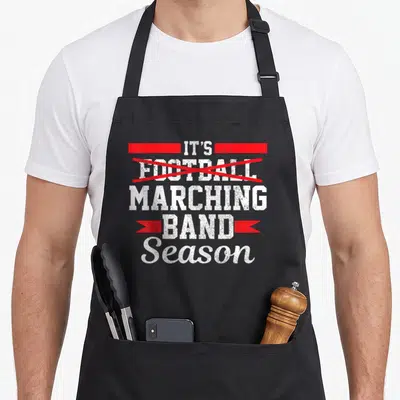 Band season football apron - Stacked white text IT'S FOOTBALL MARCHING BAND Season with red bar, X, and ribbon — shown on a black cotton canvas apron against a white background