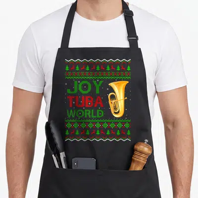Joy ugly christmas apron - Pixel art tuba with JOY TUBA WORLD text and reindeer borders in red green and gold — shown on a black cotton canvas apron against a white background