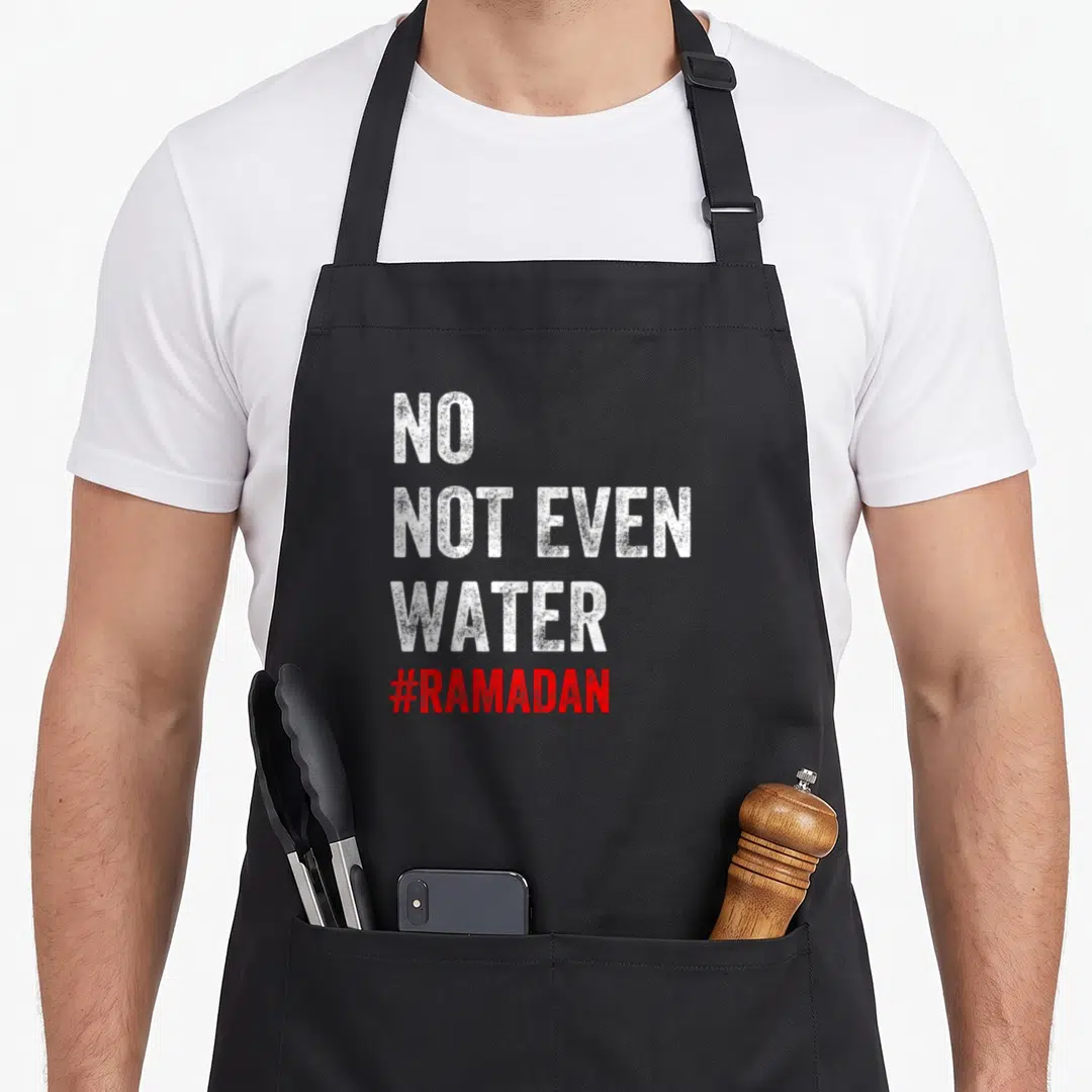 Even nourjoy apron - NO NOT EVEN WATER #RAMADAN text in white and red stacked vertically on black background — shown on a black cotton canvas apron against a white background