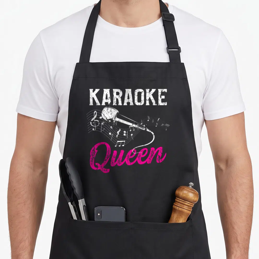 Night queen apron - Distressed white karaoke text, pink Queen script, and microphone with musical notes on black — shown on a black cotton canvas apron against a white background