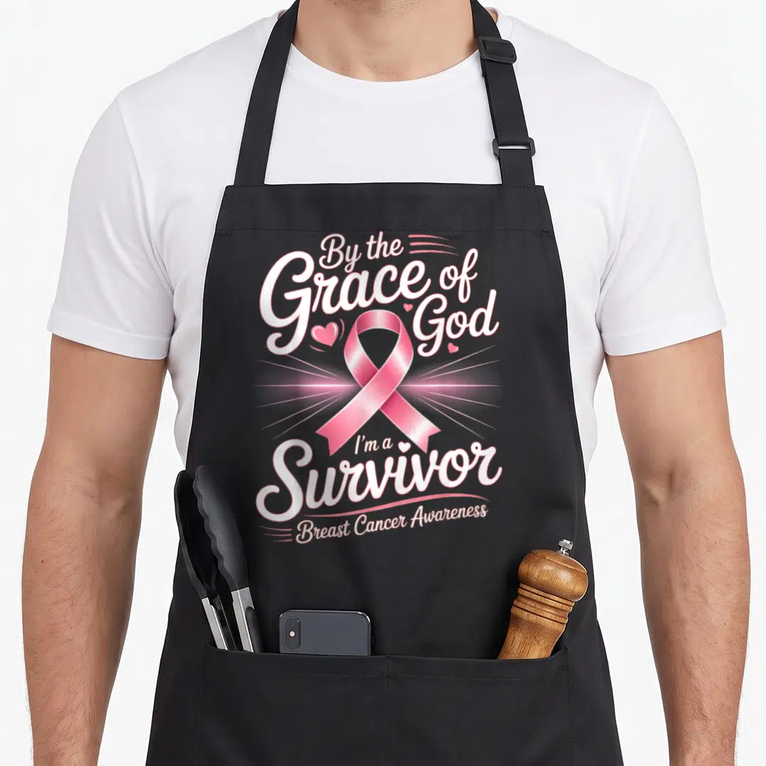 Survivor grace apron - Stacked white lettering and ribbon graphic with small hearts — shown on a black cotton canvas apron against a white background