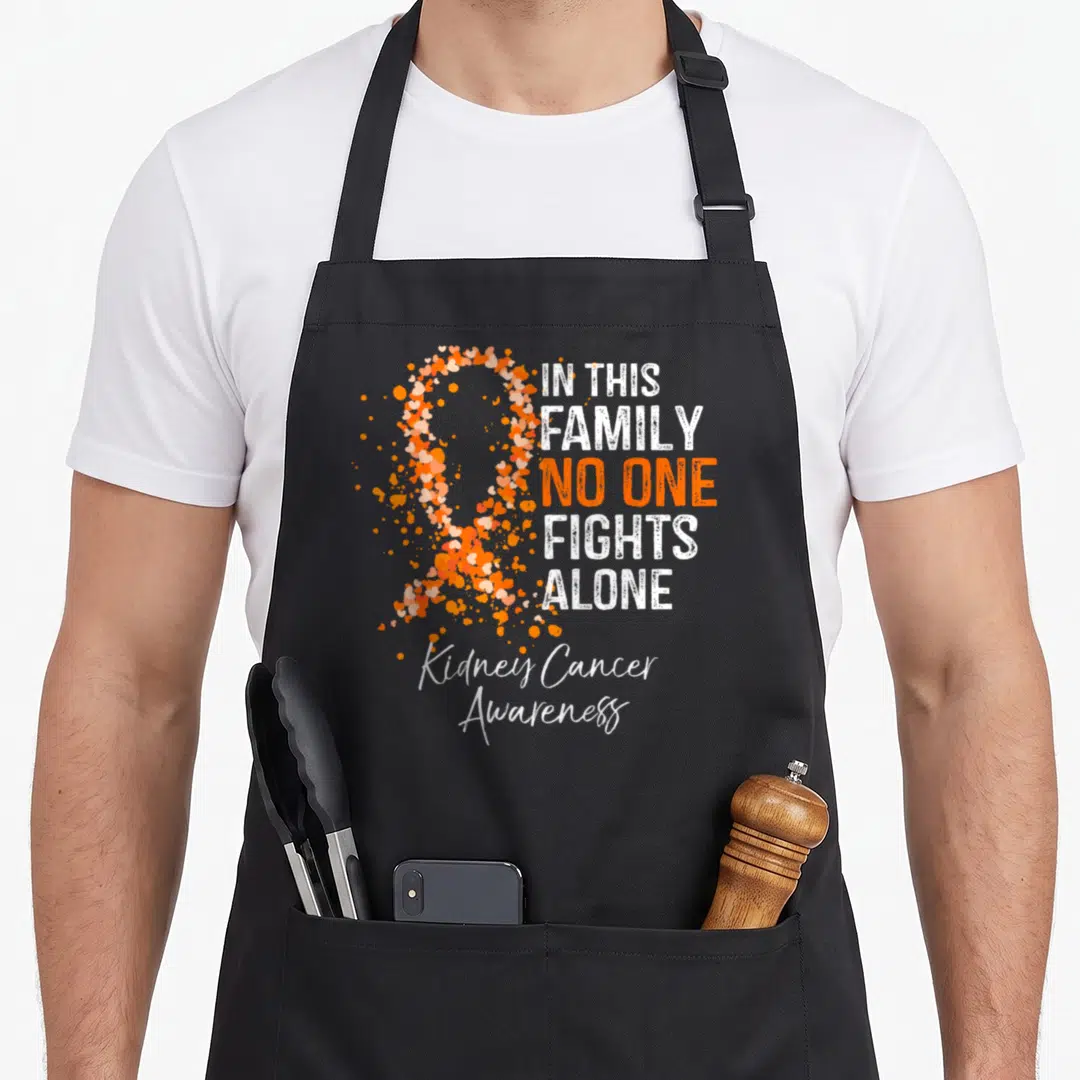 Kidney family aprons - Orange heart ribbon and white text IN THIS FAMILY NO ONE FIGHTS ALONE — shown on a black cotton canvas apron against a white background