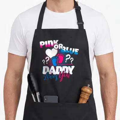 Blue husband apron - PINK OR BLUE text, heart, pink and blue footprints, and DADDY Loves You typography — shown on a black cotton canvas apron against a white background