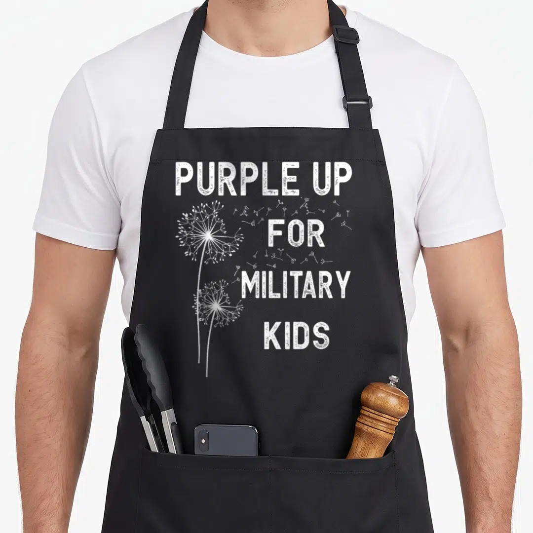 Month military apron - White distressed text purple up for military kids with two dandelions and floating seeds — shown on a black cotton canvas apron against a white background