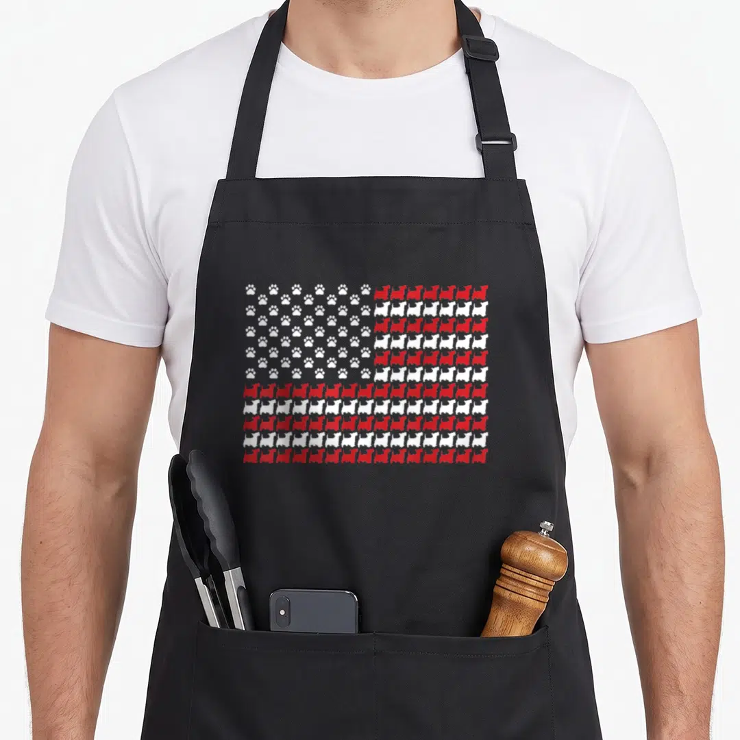 Scottie 4th of july apron - Red and white flag pattern made of rows of dog silhouettes and paw prints — shown on a black cotton canvas apron against a white background