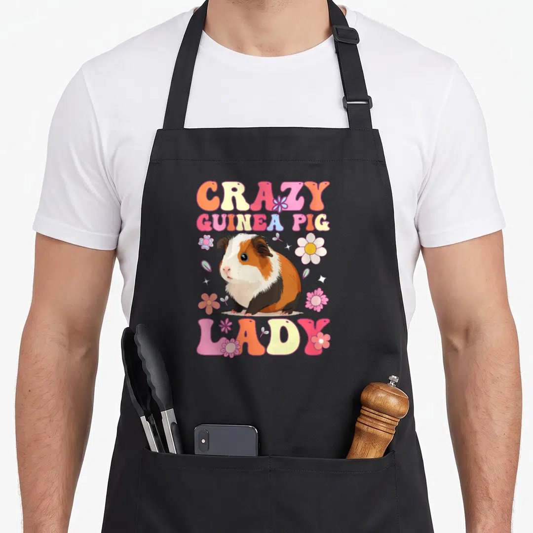 Groovy crazy guinea lady apron - Cartoon guinea pig between CRAZY GUINEA PIG LADY text with pink yellow orange flowers — shown on a black cotton canvas apron against a white background