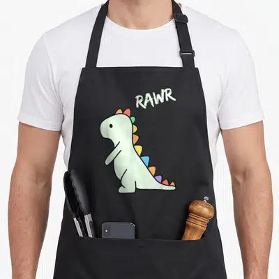 Dino cartoon apron - Light green dinosaur with rainbow spikes and angled RAWR text in cartoon style — shown on a black cotton canvas apron against a white background