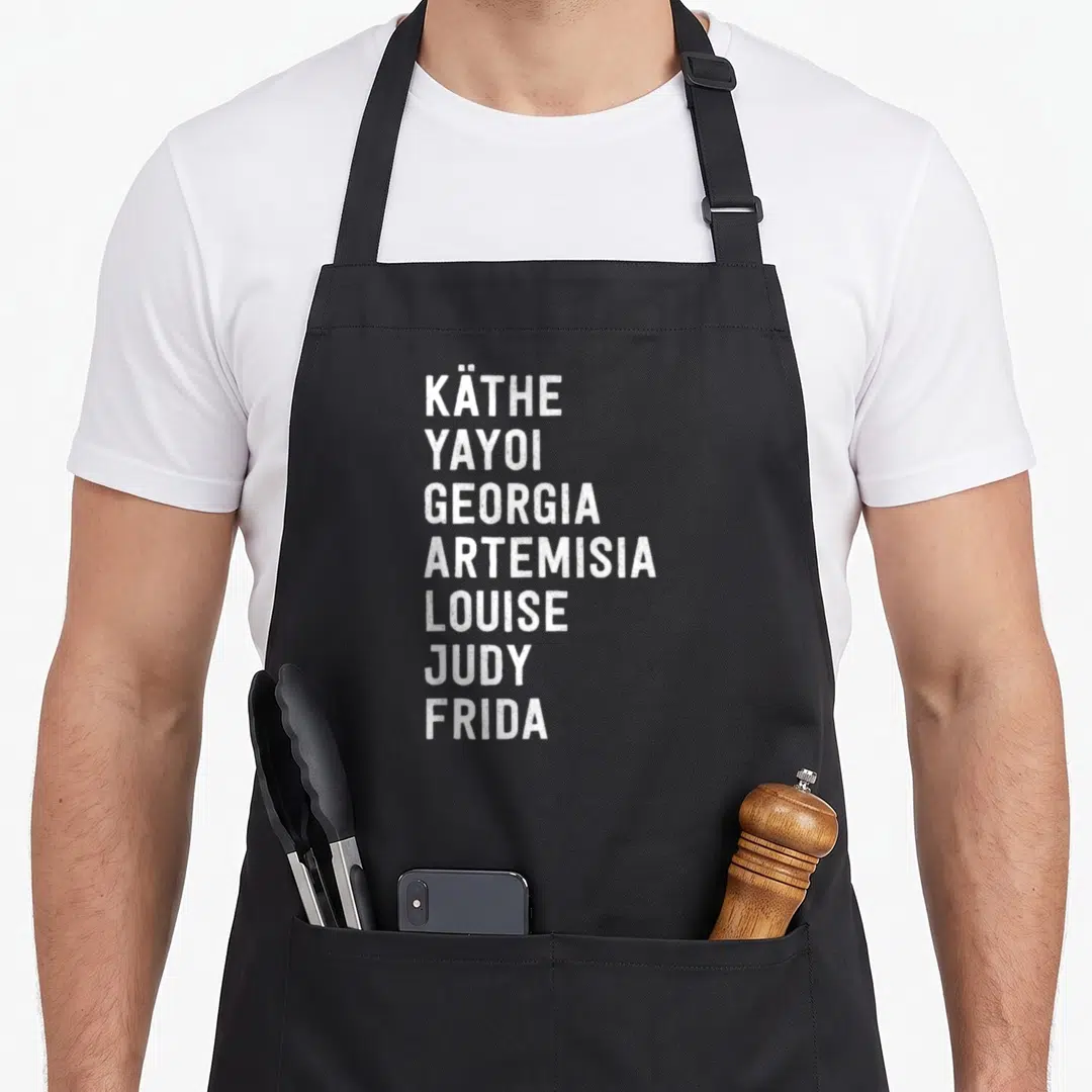 Artist famous aprons - Seven white artist names stacked vertically: Käthe Yayoi Georgia Artemisia Louise Judy Frida — shown on a black cotton canvas apron against a white background