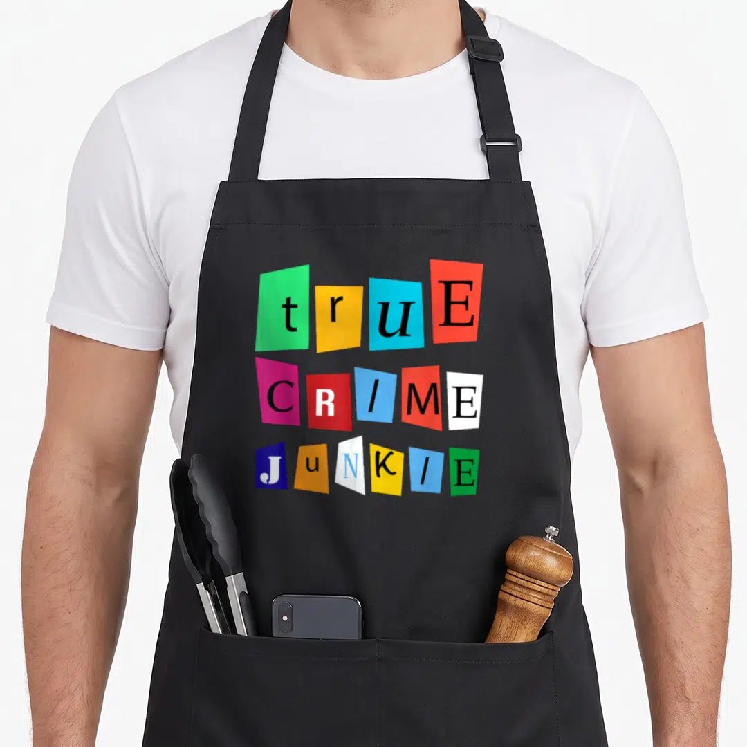 Crime podcast apron - Stacked text true CRIME Junkie on separate green, yellow, blue, red, pink, white, and black paper — shown on a black cotton canvas apron against a white background