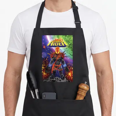 Cosmic ghost apron - Character wrapped in chains atop skulls under a planetary sky with bold yellow lettering — shown on a black cotton canvas apron against a white background