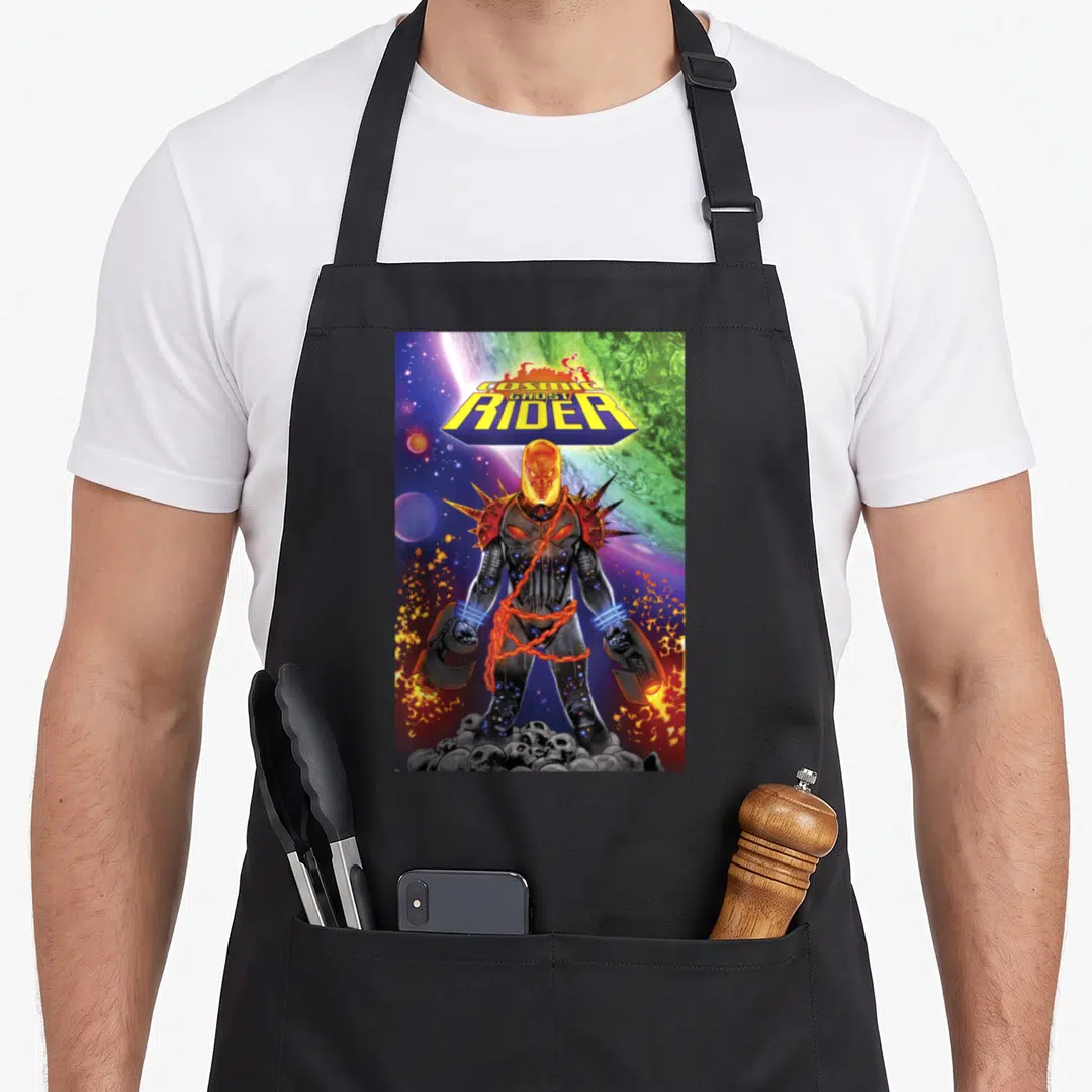 Cosmic ghost apron - Character wrapped in chains atop skulls under a planetary sky with bold yellow lettering — shown on a black cotton canvas apron against a white background