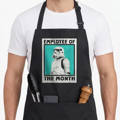 Month employee aprons - Distressed Stormtrooper inside teal rectangle with Employee of the Month text — shown on a black cotton canvas apron against a white background