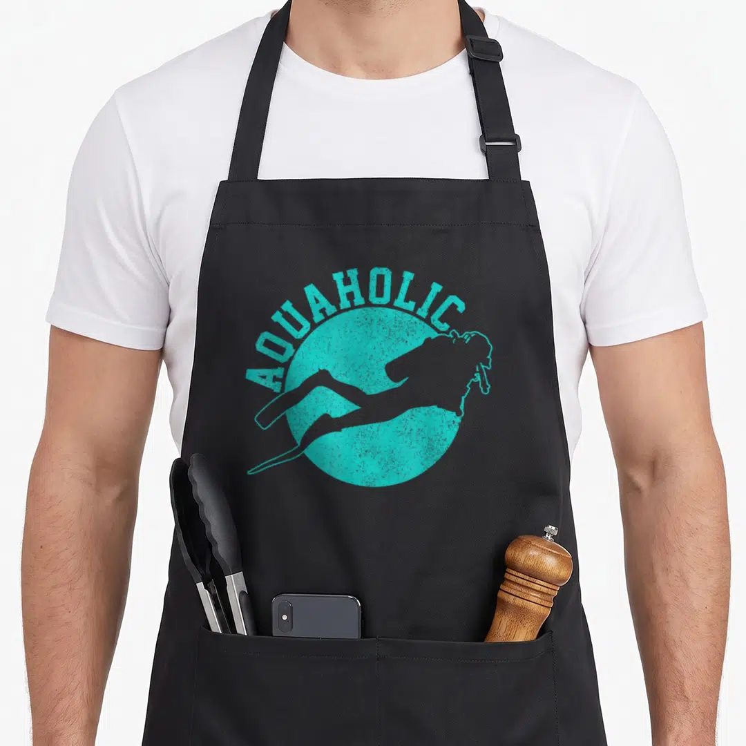 Aquaholic diving apron - Distressed AQUAHOLIC text over teal circle with white scuba diver silhouette — shown on a black cotton canvas apron against a white background