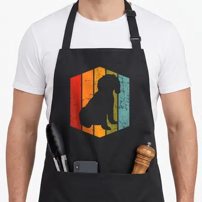 Pup cockapoo apron - Sitting dog silhouette on distressed red orange yellow and blue hexagon — shown on a black cotton canvas apron against a white background