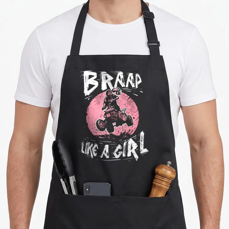 Braap quad bike apron - Distressed white BRAAAP LIKE A GIRL text arched around pink circle with ATV rider silhouette — shown on a black cotton canvas apron against a white background