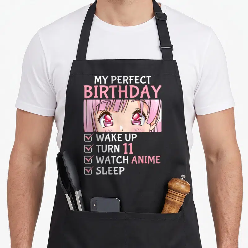 Watch anime mom apron - My Perfect Birthday text above anime girl eyes and four-item checklist in pink white red — shown on a black cotton canvas apron against a white background