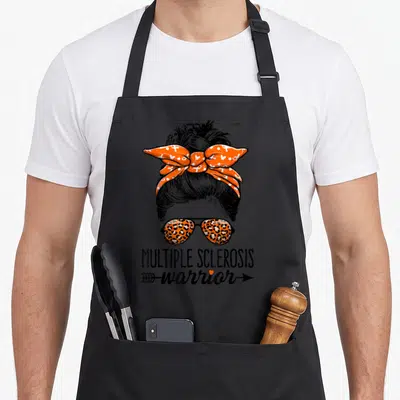 Warrior messy aprons - Cartoon woman with orange bandana and leopard sunglasses above MULTIPLE SCLEROSIS warrior text — shown on a black cotton canvas apron against a white background