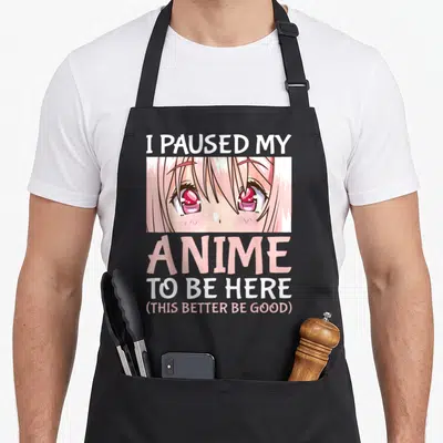 Paused anime apron - I Paused My Anime text above crying pink anime eyes in cartoon style — shown on a black cotton canvas apron against a white background