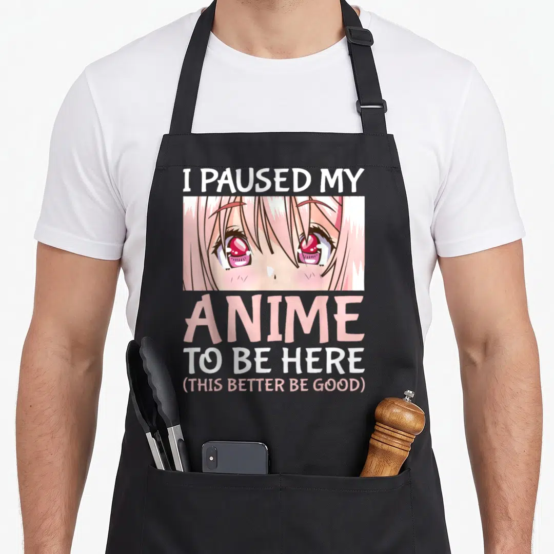 Paused anime apron - I Paused My Anime text above crying pink anime eyes in cartoon style — shown on a black cotton canvas apron against a white background