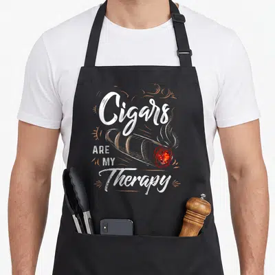Cigar my therapy apron - White typography reading Cigars Are My Therapy above a brown lit cigar with orange swirls — shown on a black cotton canvas apron against a white background