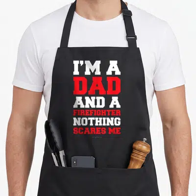 Fireman firefighter aprons - Six lines of bold white and red text reading I'M A DAD AND A FIREFIGHTER NOTHING SCARES ME — shown on a black cotton canvas apron against a white background
