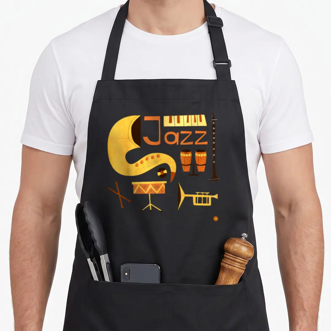 Music jazz apron - Jazz text with saxophone J, piano keys, clarinet, bongos, vinyl, snare drum, sticks, trumpet — shown on a black cotton canvas apron against a white background
