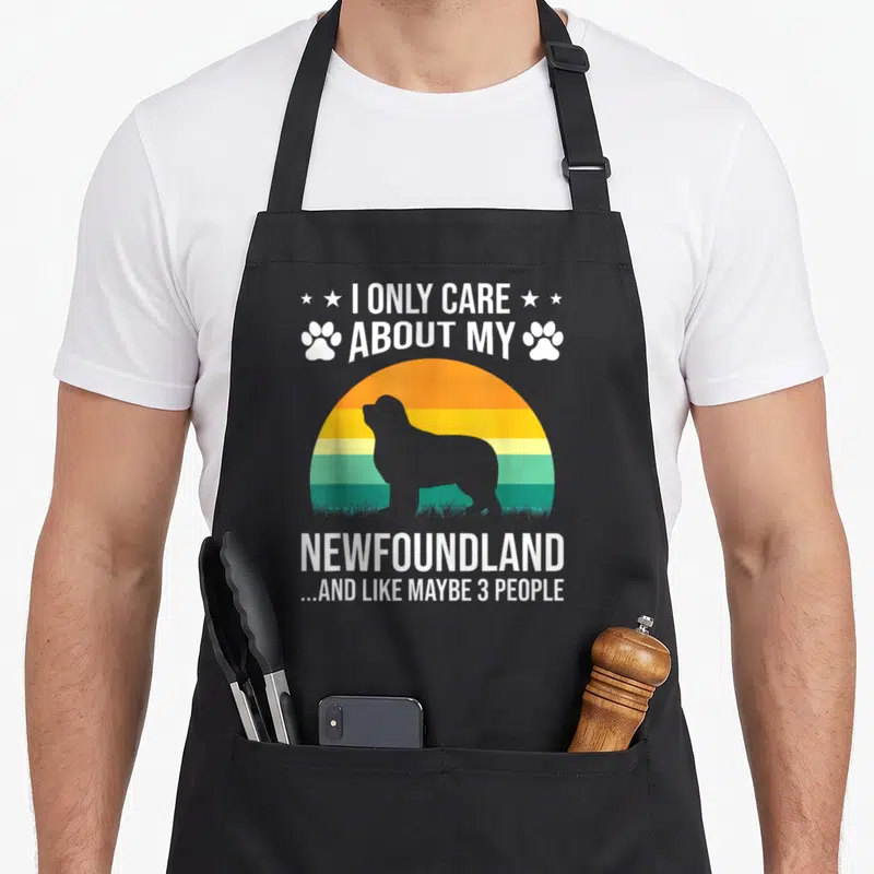 Care newfoundland dog apron - Grey Newfoundland silhouette against orange yellow and green sunset stripes with white — shown on a black cotton canvas apron against a white background