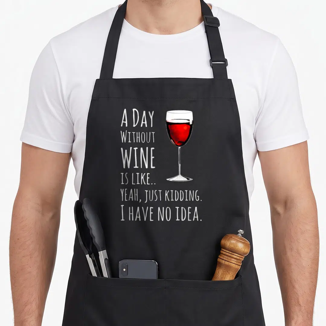 Kidding wine apron - Stacked white text reading A DAY WITHOUT WINE next to a red wine glass on black fabric — shown on a black cotton canvas apron against a white background
