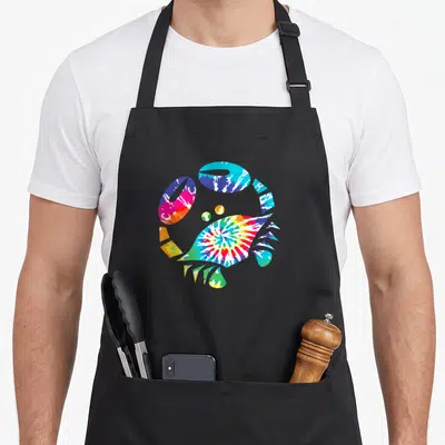 Toy crab apron - Crab silhouette filled with blue red yellow green purple tie-dye pattern — shown on a black cotton canvas apron against a white background