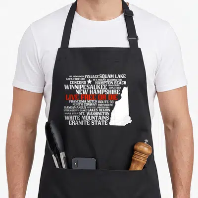 Hampshire live free apron or apron - New Hampshire map silhouette with white and red location names and Live Free — shown on a black cotton canvas apron against a white background