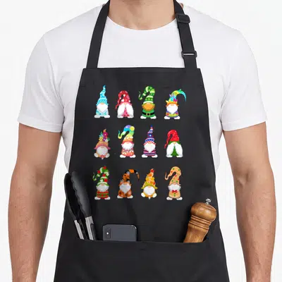 Valentine spring apron - Twelve cartoon gnomes in three rows of four wearing seasonal hats in red, green, blue, yellow — shown on a black cotton canvas apron against a white background