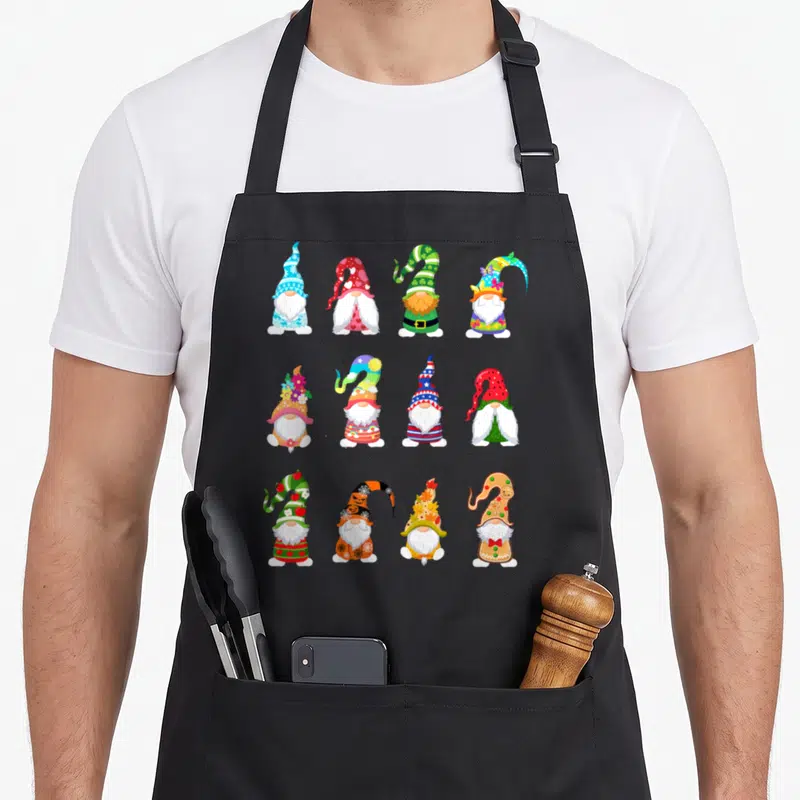 Valentine spring apron - Twelve cartoon gnomes in three rows of four wearing seasonal hats in red, green, blue, yellow — shown on a black cotton canvas apron against a white background