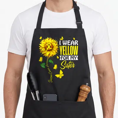 Support sarcoma awareness apron - Sunflower with ribbon and text I wear yellow for my sister sarcoma awareness — shown on a black cotton canvas apron against a white background