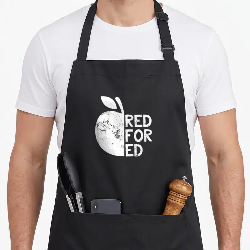 Support personalized teacher aprons - White distressed apple silhouette next to stacked RED FOR ED text — shown on a black cotton canvas apron against a white background