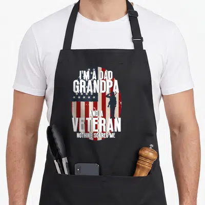 Veteran grandpa american flag apron - Distressed USA flag oval with soldier silhouette and stacked white text reading — shown on a black cotton canvas apron against a white background
