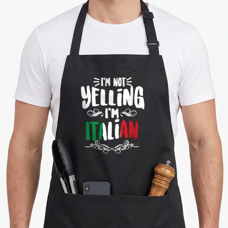 Yelling italian apron - Stacked white text reading I'M NOT YELLING I'M ITALIAN with green white red flag colors — shown on a black cotton canvas apron against a white background