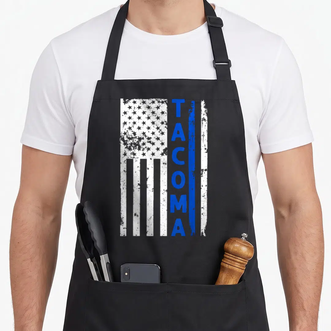 Tacoma police apron - Vertical distressed flag with TACOMA text and blue stripe — shown on a black cotton canvas apron against a white background