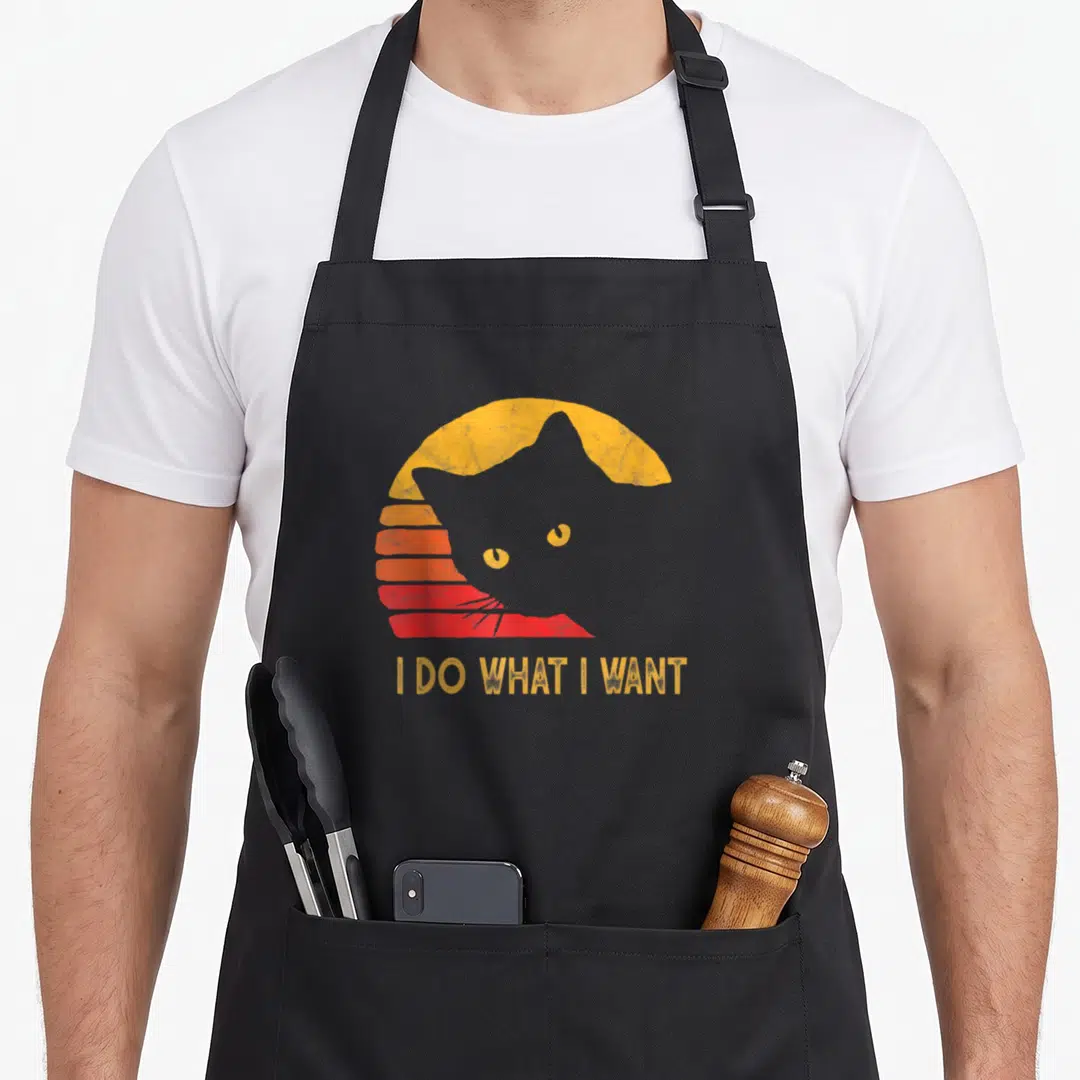 Vintage general cat apron for grilling - Grey cat silhouette against yellow orange red striped sunset with text I DO — shown on a black cotton canvas apron against a white background