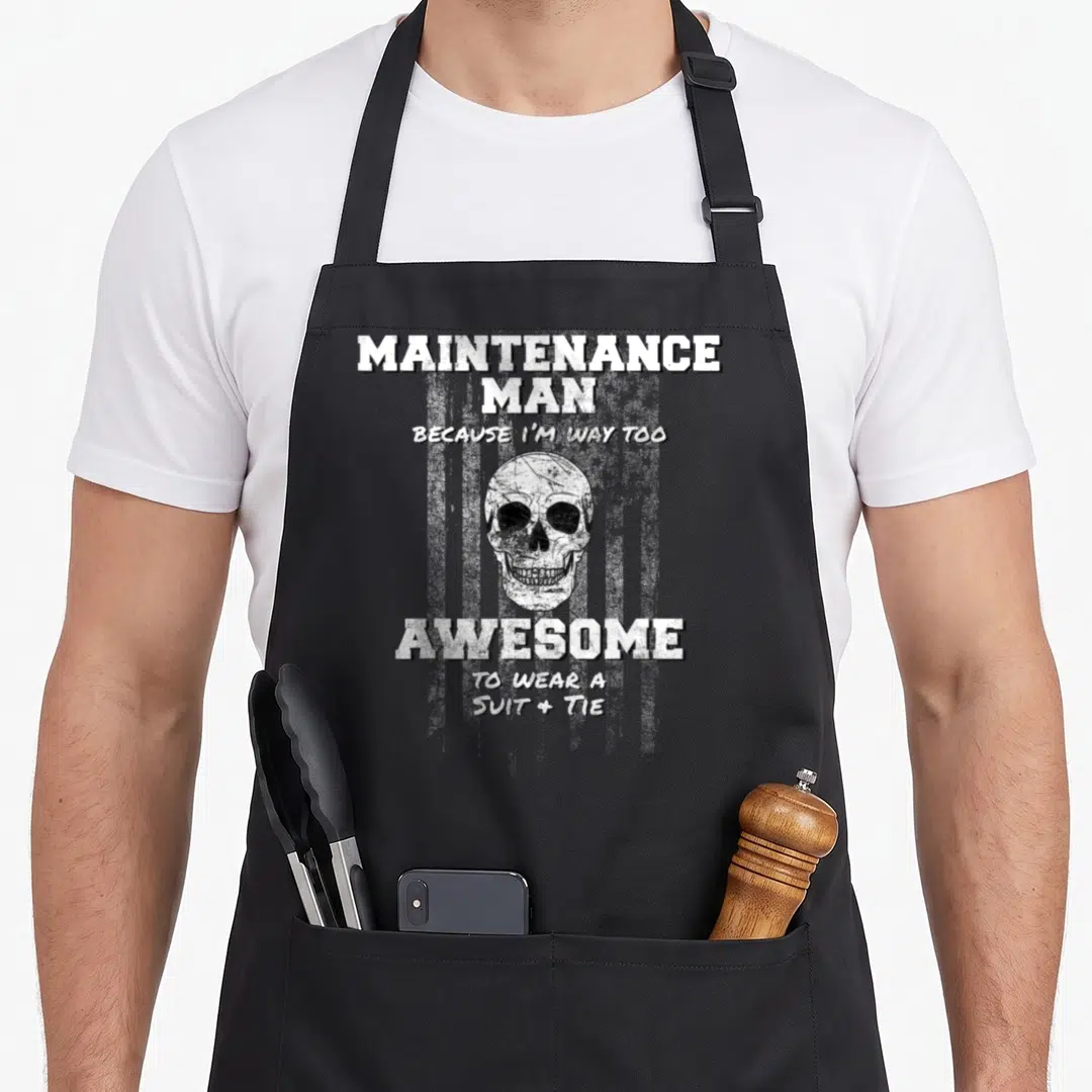 Funny supervisor maintenance apron - Distressed skull centered between MAINTENANCE MAN and AWESOME TO WEAR A SUIT + TIE — shown on a black cotton canvas apron against a white background