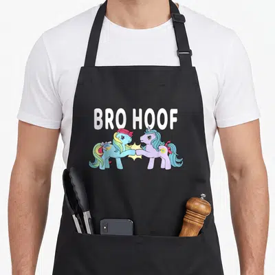 Bro rainbow apron - BRO HOOF text above two cartoon ponies touching hooves with yellow star — shown on a black cotton canvas apron against a white background