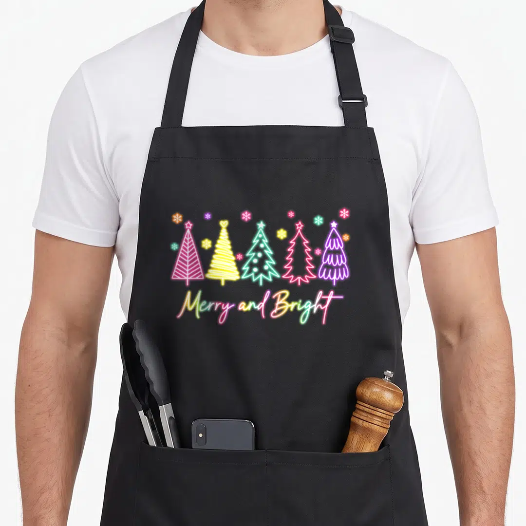 Bright christmas tree apron - Five neon Christmas trees in pink yellow teal purple red with Merry and Bright script — shown on a black cotton canvas apron against a white background