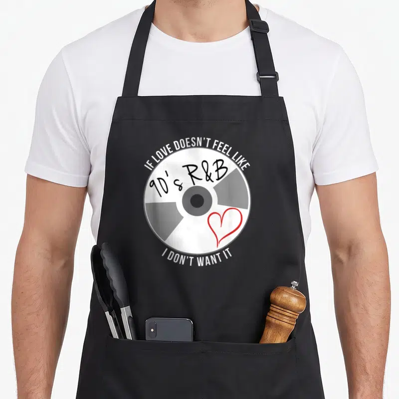 Vintage feel r aprons - CD graphic with arched text IF LOVE DOESN'T FEEL LIKE 90's R&B I DON'T WANT IT and red heart — shown on a black cotton canvas apron against a white background