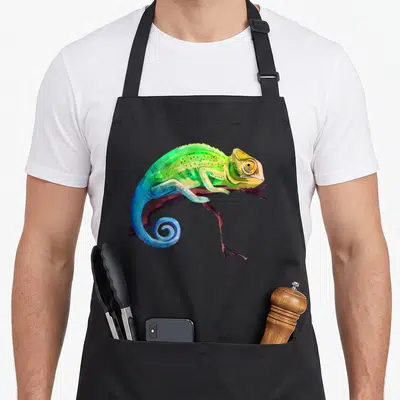 Reptile zoo animal apron - Cartoon chameleon perched on brown branch in green blue yellow and brown — shown on a black cotton canvas apron against a white background