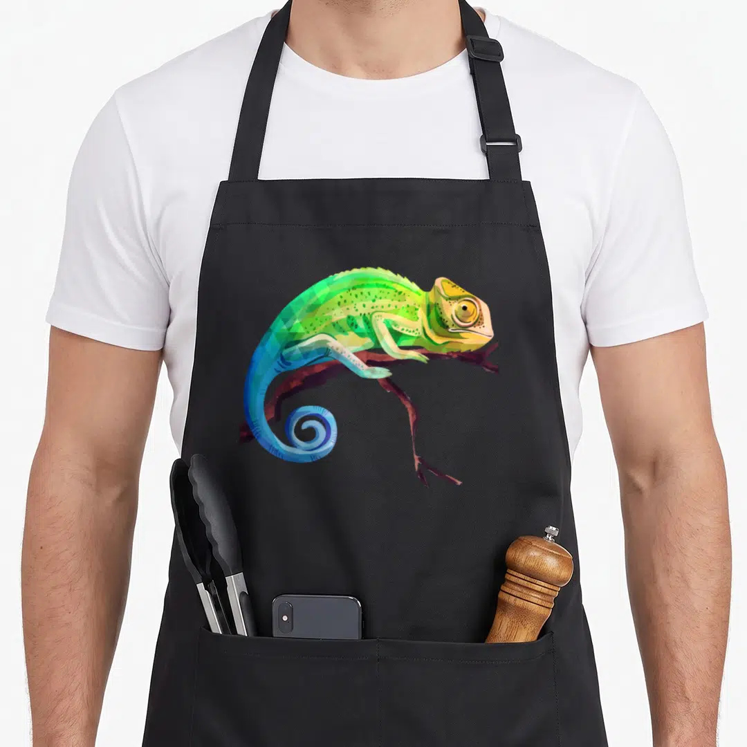 Reptile zoo animal apron - Cartoon chameleon perched on brown branch in green blue yellow and brown — shown on a black cotton canvas apron against a white background