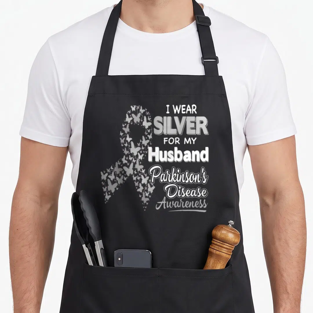 Parkinson husband apron - Silver ribbon formed by butterflies next to stacked text about wearing silver for a husband — shown on a black cotton canvas apron against a white background