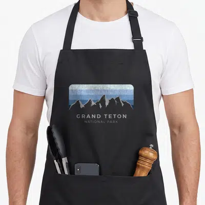 Grand winter apron - Grey mountain silhouette over blue and white horizontal bands with centered text — shown on a black cotton canvas apron against a white background