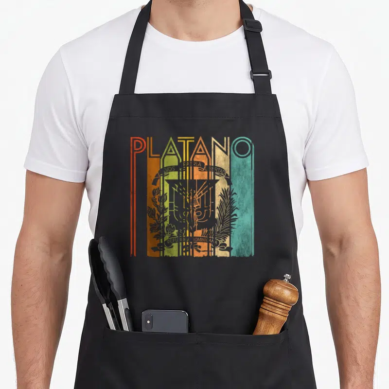 Power dominican apron - PLATANO text over Dominican coat of arms with vertical red orange yellow green blue teal stripes — shown on a black cotton canvas apron against a white background