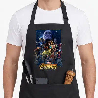 Hero infinity apron - Thanos head and Avengers cluster around Infinity Gauntlet with stacked title text at bottom — shown on a black cotton canvas apron against a white background