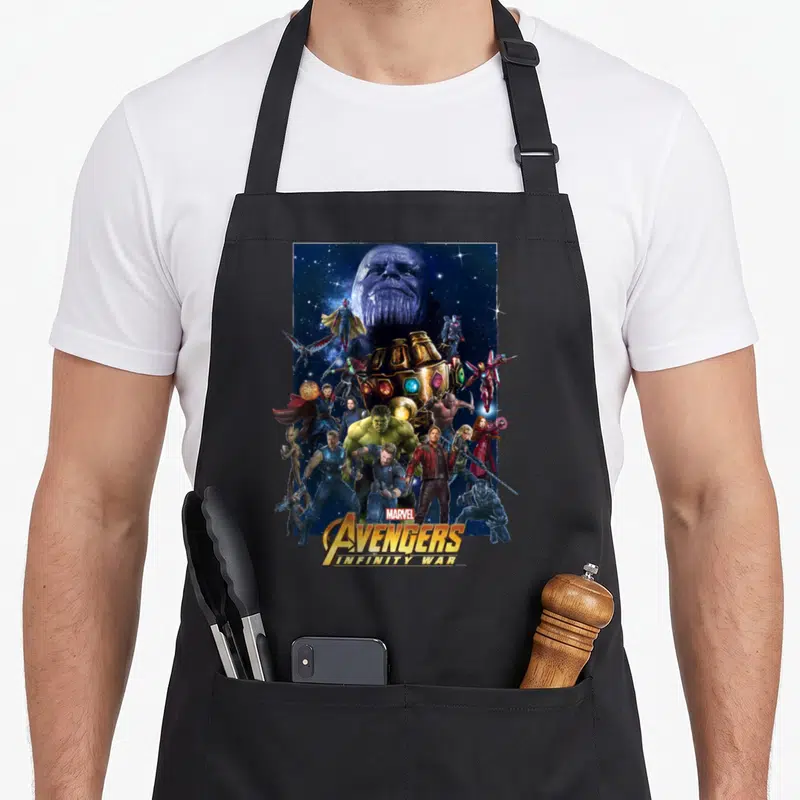 Hero infinity apron - Thanos head and Avengers cluster around Infinity Gauntlet with stacked title text at bottom — shown on a black cotton canvas apron against a white background