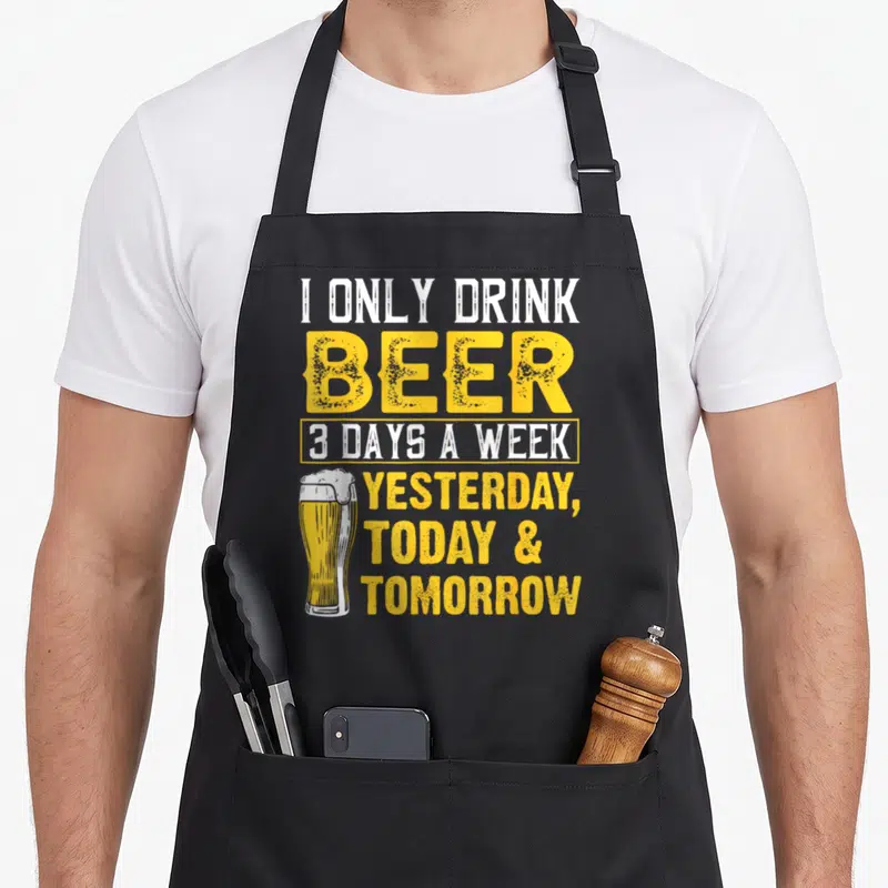 Week beer apron - I only drink beer 3 days a week text with yellow glass illustration — shown on a black cotton canvas apron against a white background